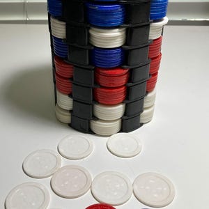 May include: A tall, cylindrical object constructed from alternating layers of blue, white, red, and black plastic discs. Several loose white, red, and blue discs are scattered in front. The object has a black top.