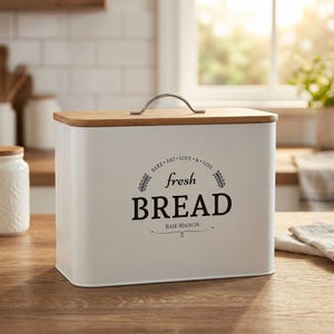 May include: A white rectangular bread box with a wooden lid and a silver handle. The words "fresh BREAD" are printed in black on the front, with the phrase "BAIE MAISON" below. The box is on a wooden surface.