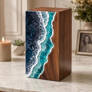 May include: A wooden box with a marine-themed design. The box has a dark wood grain finish on the sides and a resin design on the front, depicting ocean waves in shades of blue, teal, and white. The box is rectangular and sits on a marble surface.