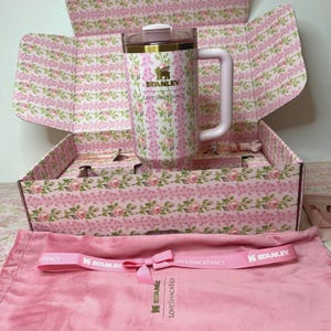 Puede incluir: Un termo de viaje Stanley LoveShackFancy rosa floral con asa, presentado en una caja a juego. El termo presenta el logotipo de Stanley y el logotipo de LoveShackFancy. Tambi&eacute;n se incluyen una correa rosa y una bolsa con cord&oacute;n rosa.