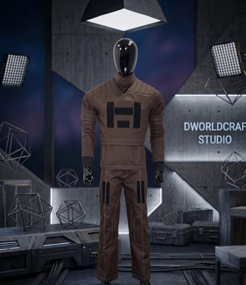May include: A brown jumpsuit with a high collar and black detailing is displayed on a mannequin. The jumpsuit has a large black graphic on the chest and contrasting stitching. The mannequin is in a studio setting with the text "DWORLDCRAFT STUDIO" visible.