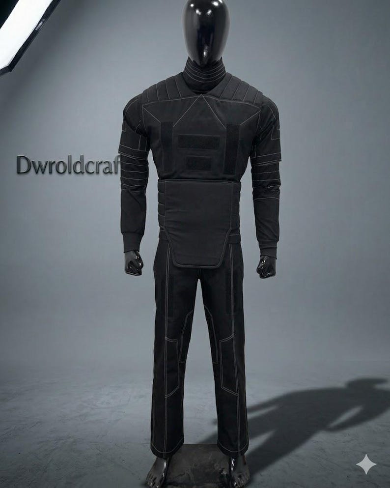 May include: Black tactical suit displayed on a mannequin. The suit features a high collar, quilted shoulders, and reinforced panels on the chest and abdomen. White stitching outlines the seams and panels. The pants have reinforced knee panels and white stitching.