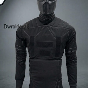 May include: Black tactical suit with a matching helmet. The suit features reinforced padding, visible stitching, and velcro patches. The helmet has a face mask with vertical vents. The mannequin is on a gray background.