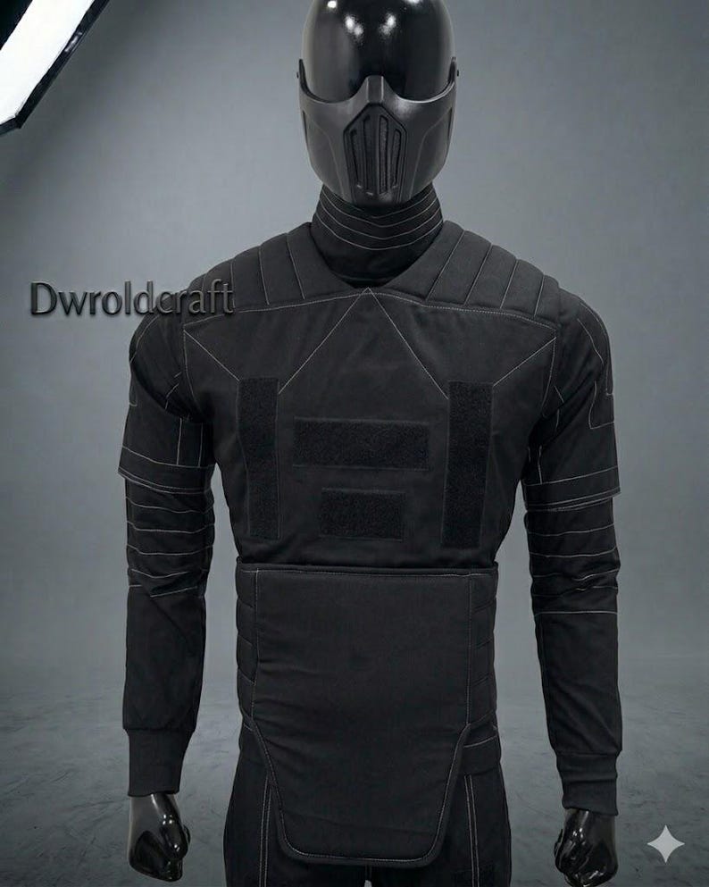 May include: Black tactical suit with a matching helmet. The suit features reinforced padding, visible stitching, and velcro patches. The helmet has a face mask with vertical vents. The mannequin is on a gray background.