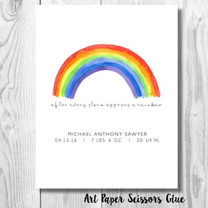May include: A watercolor print featuring a vibrant rainbow arching over the phrase "after every storm appears a rainbow." Below, the print includes a name, date, weight (7 lbs. 6 oz.), and length (20 1/4 in.). The bottom right corner reads "Art Paper Scissors Glue."