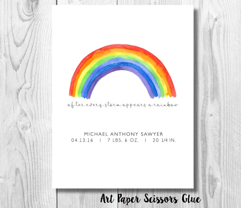 May include: A watercolor print featuring a vibrant rainbow arching over the phrase "after every storm appears a rainbow." Below, the print includes a name, date, weight (7 lbs. 6 oz.), and length (20 1/4 in.). The bottom right corner reads "Art Paper Scissors Glue."