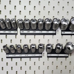 May include: A collection of silver-colored metal socket wrench attachments arranged on black magnetic organizers. The set includes metric sizes from 10mm to 34mm and imperial sizes from 3/8 inch to 3/16 inch, with each size clearly labeled on the base.