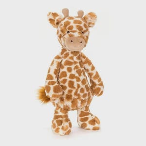 May include: A plush giraffe toy with a soft, textured body. The giraffe features a brown and white spotted pattern, a tan snout, small ears, and a fluffy tail. The toy is designed to stand upright and is suitable for children.