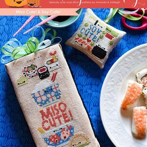 May include: Two cross stitch patterns on fabric, one with the text "Miso Cute!" and the other with the text "Soy Cute!" The patterns are on a blue background with a plate of sushi in the background.