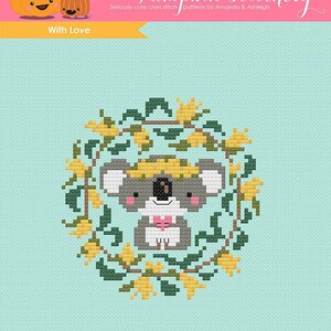 Könnte beinhalten: Kreuzstichmuster mit einem niedlichen Koala, der eine Blumenkrone trägt und ein Herz hält. Der Koala ist von einem Kranz aus gelben Blumen und grünen Blättern umgeben. Das Muster ist auf einem hellblauen Hintergrund. Das Logo von The Frosted Pumpkin Stitchery befindet sich in der oberen linken Ecke.