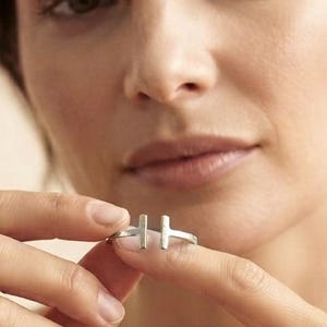 May include: A silver-toned open ring featuring two vertical bar elements positioned at the centre of the band. The ring has a smooth, polished finish and a minimalist design with a gap between the two parallel bars, creating a clean aesthetic.