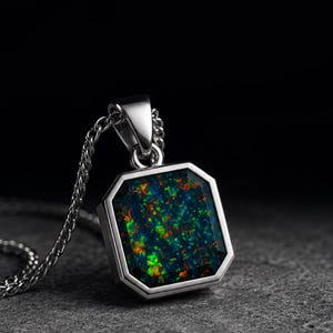 Könnte beinhalten: Eine silberfarbene Anhängerkette mit einem achteckigen schwarzen Opal-Edelstein. Der Stein zeigt lebhafte rote, orangefarbene und grüne Farbspiele. Der Anhänger hängt an einer passenden silberfarbenen Metallkette mit Gliedern.