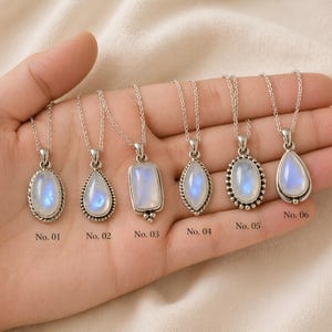 May include: Six silver necklaces with iridescent moonstone pendants in various shapes: oval, teardrop, and rectangular. Each pendant is set in a silver bezel and hangs from a delicate chain. The pendants are labeled with numbers.