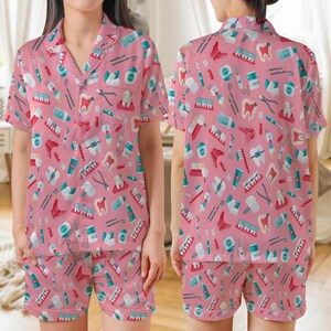 Puede incluir: Conjunto de pijama rosa con un estampado de herramientas dentales, dientes y cepillos de dientes. La parte superior de manga corta tiene cuello y cierre de botones. Los pantalones cortos a juego completan el conjunto. La ropa de dormir con temática dental está hecha de un material suave.