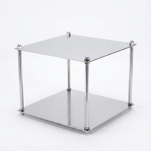 May include: A two-tiered, square, stainless steel display stand. The stand has a polished finish, with four cylindrical legs connecting the top and bottom platforms. Each leg is capped with a decorative, rounded element. The stand is suitable for displaying items.