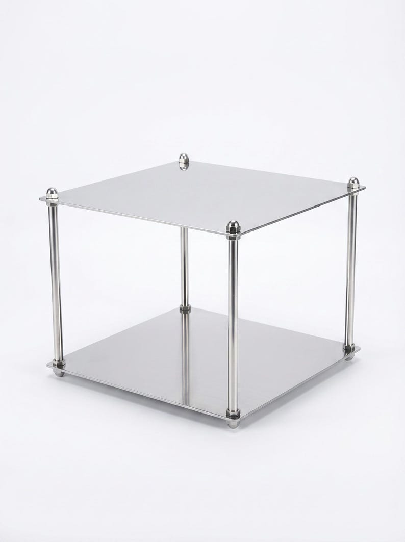 May include: A two-tiered, square, stainless steel display stand. The stand has a polished finish, with four cylindrical legs connecting the top and bottom platforms. Each leg is capped with a decorative, rounded element. The stand is suitable for displaying items.