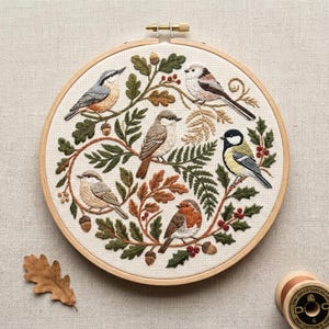 May include: Embroidered hoop art featuring six detailed birds perched on branches with leaves, acorns, and berries. The birds are in shades of brown, gray, and yellow, set against a cream-colored fabric. The wooden hoop is approximately 8 inches in diameter.
