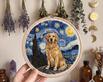 Puede incluir: Un bastidor de bordado circular de madera que contiene un retrato detallado cosido con hilo de un perro golden retriever. El perro está centrado sobre un fondo inspirado en un cielo estrellado con patrones azules arremolinados, estrellas amarillas y un ciprés oscuro.