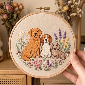 Puede incluir: Arte de aro bordado con tres perros: un golden retriever, un beagle y un dachshund. Los perros están rodeados de flores bordadas, incluyendo margaritas, lavanda y rosas, con acentos de setas. El aro es de madera.