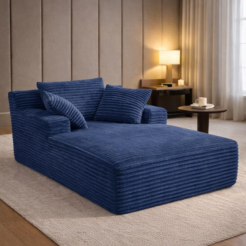 Deep blue corduroy chaise lounge with plush cushions and modern low-profile design, styled in a cozy bedroom setting.