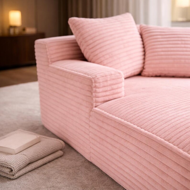 Pink corduroy chaise lounge sofa with wide armrest and matching pillows, styled in a warm, modern bedroom interior.
