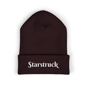 May include: A dark burgundy beanie with the word "Starstruck" embroidered in white script across the front. The beanie is a classic, close-fitting style, suitable for cold weather.