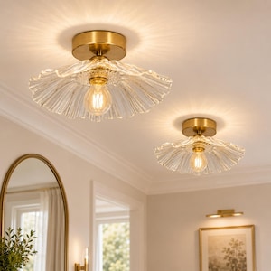 May include: Two flush mount ceiling lights featuring circular brass bases and wide, scalloped clear glass shades with a ribbed texture. Each fixture holds a single glowing light bulb in the center, casting a warm, radial light pattern.
