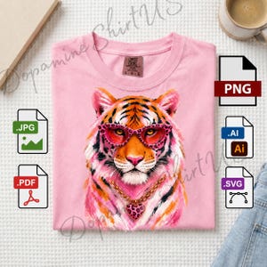 May include: A light pink t-shirt featuring a graphic illustration of a tiger wearing pink leopard-print glasses and a gold chain with a heart-shaped pendant. The shirt has a crew neckline and a Comfort Colors brand label on the inside collar.