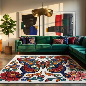 May include: A living room with a green sectional sofa, a large butterfly rug, and abstract art. The rug features a colorful butterfly design with red, blue, and orange accents. The room also includes a wooden cabinet and potted plants.