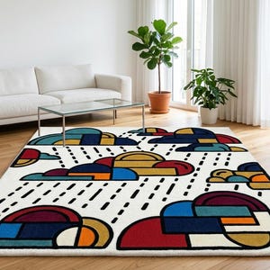 Pode incluir: Um tapete retangular com um design de nuvens. O tapete apresenta um fundo branco com formas de nuvens coloridas em vermelho, azul, amarelo e preto. Linhas pretas representam a chuva. O tapete est&aacute; colocado sobre um ch&atilde;o de madeira.