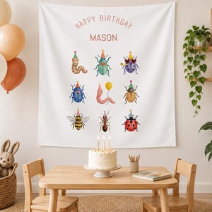 Peut inclure: Une tapisserie murale en tissu blanc avec le texte HAPPY BIRTHDAY MASON en lettres rouges, ornée d'illustrations à l'aquarelle de neuf insectes portant des chapeaux de fête, dont un ver, un scarabée, une abeille, une fourmi et une coccinelle.