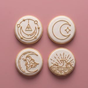 May include: Four round cookies with white icing and gold-colored designs. The designs include a crescent moon with a star, a sun over waves, a crescent moon with clouds, and a symbol with a triangle and stars.
