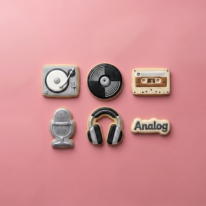 May include: A set of six music-themed cookies shaped like a turntable, a vinyl record, a cassette tape, a microphone, headphones, and a cookie with the word Analog written in dark gray icing. Each cookie features detailed icing designs.