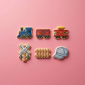 May include: A set of six decorated sugar cookies featuring a blue locomotive, a red freight car, a red caboose, a white railroad crossing sign with the text RAIL CROSSING ROAD, a brown wooden fence, and a white and blue striped conductor hat.