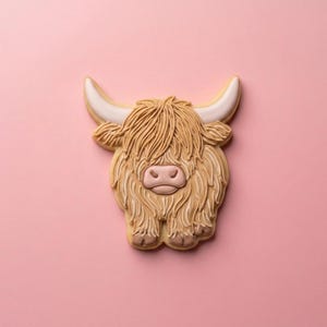May include: A Highland cow cookie with tan fur, a pink nose, and white-tipped horns. The cookie is set against a solid pink background. The cookie is decorated with detailed icing.