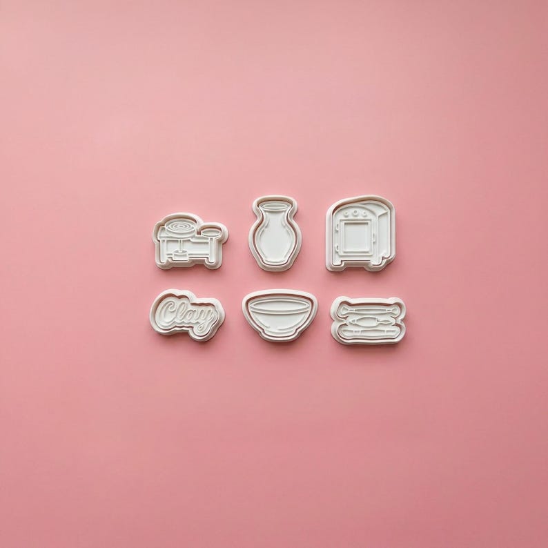 May include: A set of six white plastic cookie cutters featuring pottery-themed shapes including a pottery wheel, a vase, a kiln, the word Clay in cursive script, a bowl, and a collection of sculpting tools arranged in two rows of three.