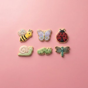 May include: Six insect-shaped sugar cookies arranged in two rows. The top row features a yellow and black bee, a purple and blue butterfly, and a red and black ladybug. The bottom row includes a light pink snail, a green caterpillar, and a dragonfly.