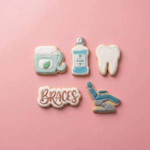 May include: A set of five dental-themed cookies decorated with icing. The shapes include a light blue dental floss container, a bottle of mouthwash labeled MINT RINSE, a white tooth, a cookie with the word BRACES, and a blue dental chair.