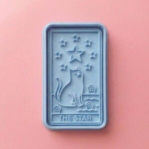 May include: A light blue rectangular mold featuring a cat silhouette, stars, and paw prints. The text "THE STAR" is at the bottom. The mold is set against a pink background.