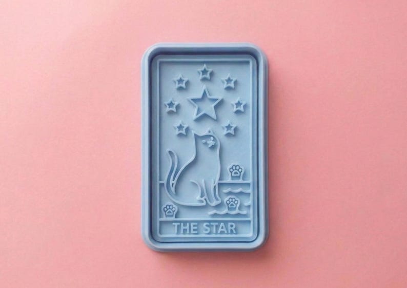 May include: A light blue rectangular mold featuring a cat silhouette, stars, and paw prints. The text "THE STAR" is at the bottom. The mold is set against a pink background.