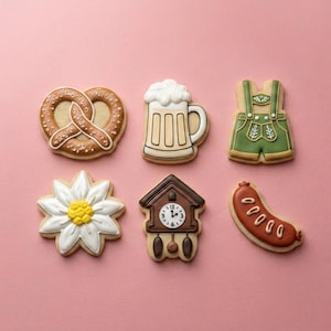 May include: Six decorated sugar cookies arranged in two rows. The top row features a brown pretzel, a beer mug with white foam, and green lederhosen. The bottom row includes a white daisy, a brown cuckoo clock, and a brown sausage link.