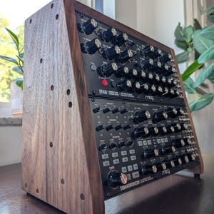 以下が含まれることがあります： ダークウッド製の2段式シンセサイザー用スタンドに、黒いMoogユニットが2台収められています。上段のユニットにはDFAM、下段のユニットにはSUBHARMONICONと記されています。どちらも多数の黒いコントロールノブと白いテキストラベルが特徴です。