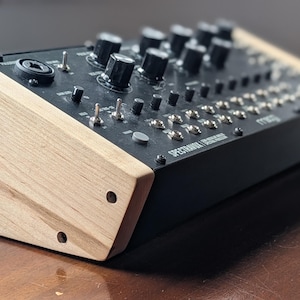 May include: A black synthesizer with wooden side panels. The device features numerous knobs, switches, and inputs. The text "SPECTRAVOX / SOUND STUDIO" is visible on the front panel. The synthesizer is designed for music production and sound design.