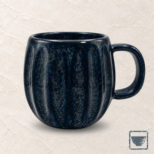 Op de afbeelding: Een donkerblauwe keramische mok met een afgerond, geribbeld lichaam en een glanzende, gespikkelde afwerking. De mok is voorzien van een gebogen handvat aan de rechterkant en een diep, gemêleerd kleurenpalet met lichtere blauwe accenten.