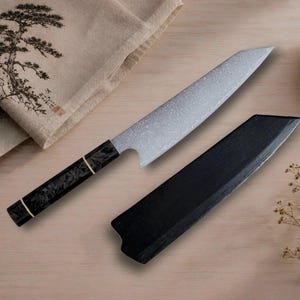 Può includere: Un coltello da chef in stile giapponese con una lama in metallo argentato testurizzato e un manico scuro a motivi decorato con due sottili anelli dorati. Accanto al coltello si trova un fodero in legno nero abbinato dal design affusolato.