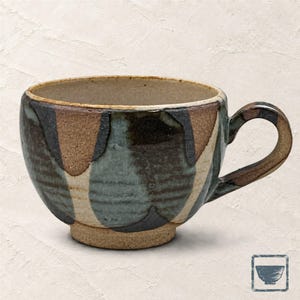 Può includere: Una tazza in ceramica con un corpo largo e arrotondato e un manico curvo. L'esterno presenta un motivo dipinto a mano di forme verticali sovrapposte in tonalità di blu tenue, marrone scuro e terra, con una base ruvida non smaltata.