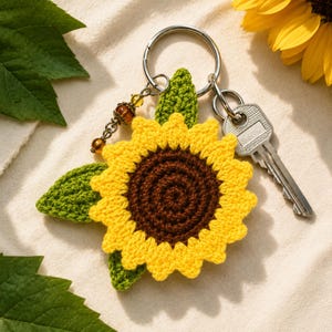May include: A handmade crochet sunflower keychain with a yellow and brown flower, green leaves, and a silver key ring. The keychain includes a decorative beaded charm and a silver key. The sunflower measures approximately 3 inches in diameter.