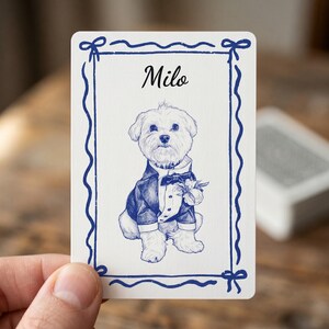 May include: A white playing card featuring a blue ink sketch of a small dog wearing a tuxedo with a bow tie and a flower boutonniere. The name Milo is printed in black script above the dog, all enclosed within a blue decorative ribbon border.