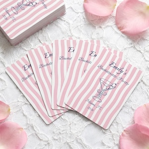 May include: A stack and a fan of rectangular cards featuring a pink and white vertical wavy stripe pattern. Each card displays a dark blue line drawing of a martini glass with olives, the text Emily's Bachelorette Party, and Miami, FL 2026.