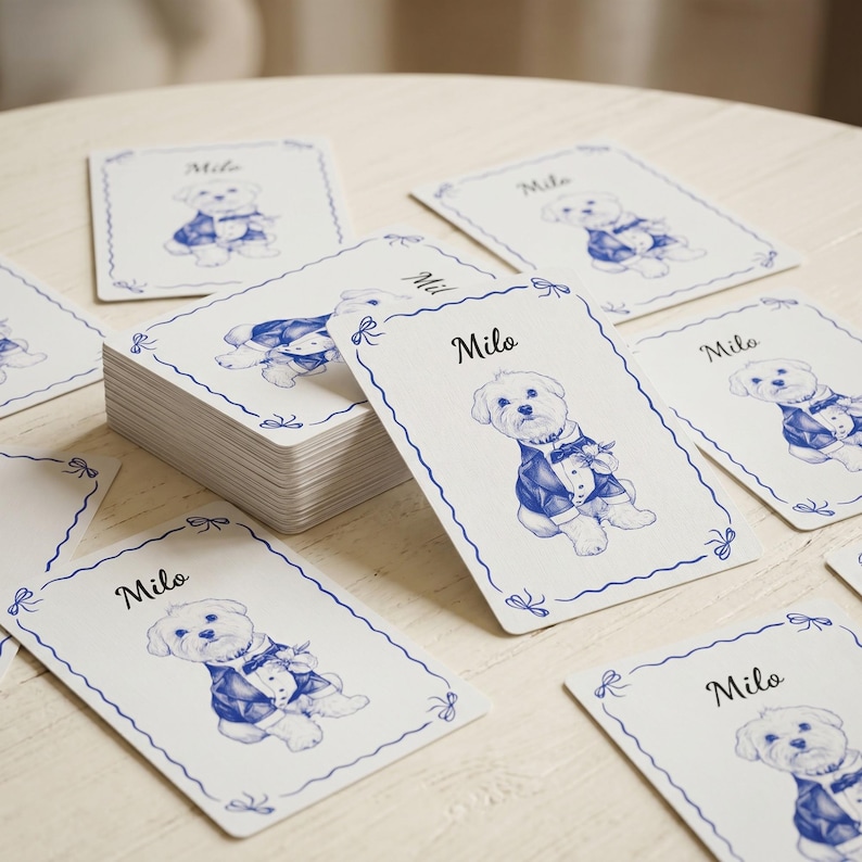 May include: A stack and scattered collection of rectangular white cards featuring a blue ink illustration of a dog wearing a tuxedo and the name Milo printed in black script. Each card has a decorative blue wavy border with small bow accents.